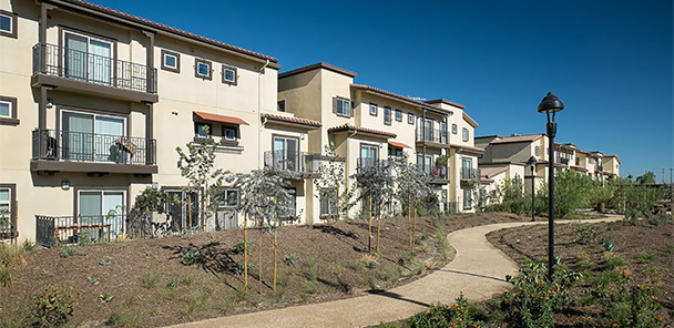 Three-story stucco apartment building with balconies overlooking curvilinear concrete sidewalk.